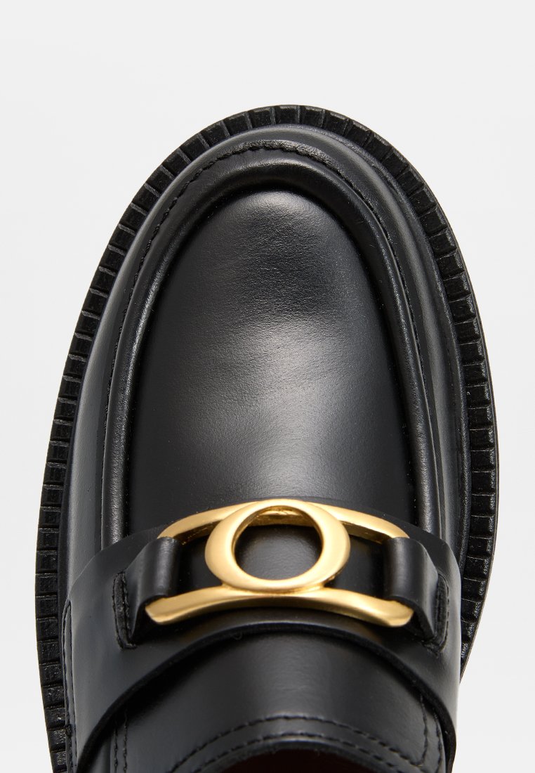 Schwarze Lederloafer mit glänzender Oberfläche, ausgestattet mit einem goldenen runden Akzent auf einem schwarzen Riemen. Die Sohle hat strukturiertes schwarzes Detail.