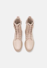 Beige läderankelboots med snörning, sidodragkedja och dekorativ sömnad. Rundad tå och texturerad sula för bra grepp.