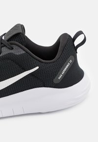 Pantof cu aspect sportiv, de culoare neagră, cu un superior din țesătură texturată, accente albe și o talpă flexibilă. Are eticheta "Flex Experience 12" pe lateral.