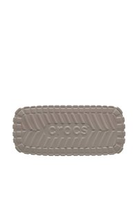 Semelle de Crocs beige clair présentant un motif de semelle texturé, des bords arrondis et un logo "CROCS" en relief au centre. Matière en plastique lisse.