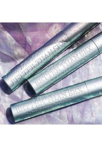 Drie metallic paarse mascara tubes met reliëftekst, met waterdruppels op het oppervlak. Het ontwerp is slank en cilindrisch.