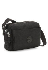 Sort nylon crossbody taske med lynlås, justerbar rem og en gummimonkey-nøglering. Har en rund logopatch foran.