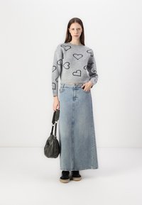 Grå genser med svarte hjerte-design, parret med et lyseblått denim maxiskjørt. Modellen holder en svart veske, iført svarte joggesko med beige såler.
