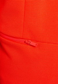 Tissu rouge vif à texture côtelée avec une poche zippée. La fermeture éclair est assortie à la couleur, offrant un aspect homogène.