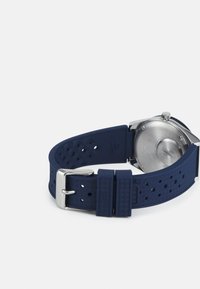 Navy blue rubber watch strap featuring a textured pattern, silver metal buckle, and a stainless steel back.