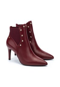 Botas de tobillo de cuero burdeos con punteras afiladas, laterales en forma de V, paneles elásticos y tachuelas doradas decorativas a lo largo de la costura exterior. Tacones de 3 pulgadas.
