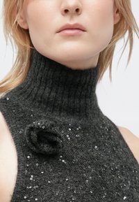 Charcoal grey, high-neck sleeveless knit top with a textured finish, embellished with sequins and a fabric flower detail on the shoulder.