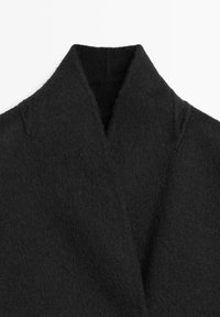 Cappotto di lana nera con colletto strutturato, caratterizzato da un tessuto morbido e texture piacevole, con dettagli di design puliti e minimalisti.