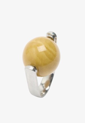 Srebrny pierścionek z szeroką obrączką, trzymający dużą, gładką, okrągłą musztardowo-żółtą kamień osadzony na białym tle.