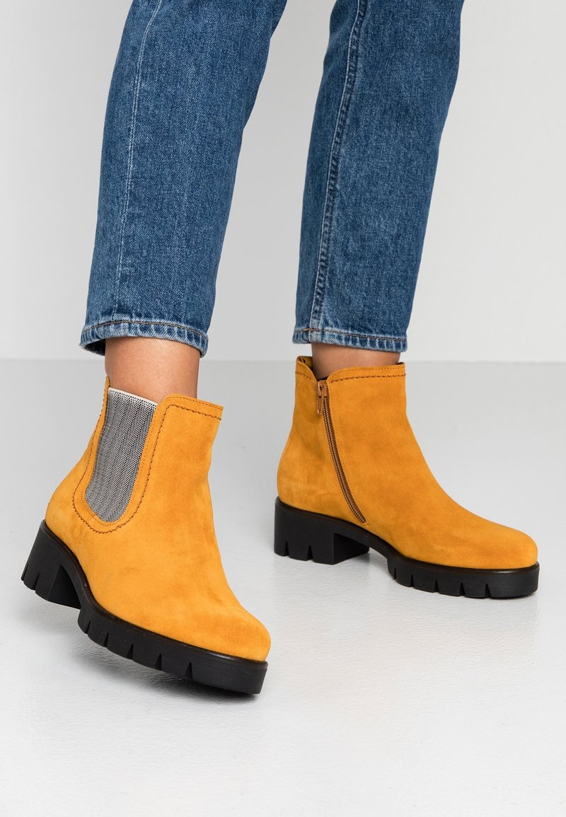 Bottes de cheville en suede jaune avec une semelle noire robuste, dotées de panneaux latéraux élastiques et d'une fermeture éclair d'un côté.