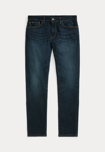 Tamnoplave uske traperice s blagim izblijedjenjem i dizajnom s pet džepova, položene ravno na bijeloj pozadini.