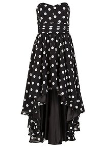 Robe noire bustier à pois blancs, taille froncée et jupe superposée asymétrique plus longue à l'arrière qu'à l'avant.
