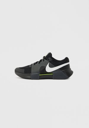 Fekete és szürke sportcipő fehér Nike pipa logóval, neon zöld részlettel a középtalpon, hálós felsőrészen és texturált talpon.