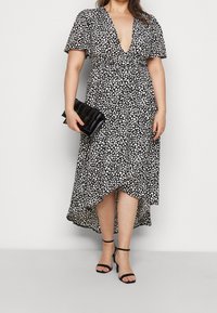 Czarna sukienka w białe kropki, z głębokim dekoltem w serek, krótkimi rękawami i asymetrycznym dołem. W zestawie czarna kopertówka i sandały na obcasie z paskami.