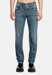 Blue denim jeans with a slim fit, featuring a faded wash, five pockets, and stitching accents. Worn with black ankle boots.