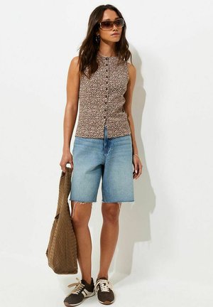 Femme portant un haut sans manches à imprimé léopard, un short en jean, des lunettes de soleil et des baskets, tenant un sac fourre-tout tissé marron.