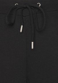 Czarne spodnie dresowe z fasonem typu drawstring, wykonane z gładkiego materiału, z oczkami typu grommet oraz metalowymi końcówkami w kolorze srebrnym na sznurku dla dodatkowego detalu.