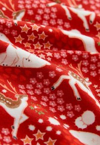 Piros anyag ünnepi mintával, amelyen rénszarvasok, csillagok és apró virágok találhatóak fehér, barna és rózsaszín részletekkel.
