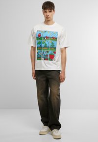 Hvit bomull-t-skjorte med et fargerikt tegneserie-illustrasjon i paneler som skildrer planter og en smilende jordbær, kombinert med mørk denimjeans.