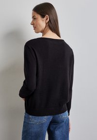 Maglione nero a maglia con vestibilità morbida, scollo ampio e orlo a costine. Abbinato a jeans in denim blu chiaro. Design semplice e testurizzato.