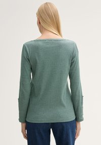 Groene langemouwenshirt met een ronde halslijn en een textuur gestreept patroon. De stof lijkt zacht; heeft een comfortabele pasvorm en knoopaccenten.