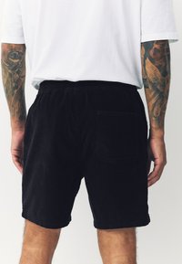 Zwarte corduroy shorts met een elastische tailleband en een achterzak, voorzien van een textuur met ribbels, gecombineerd met een wit t-shirt.
