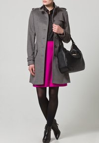 Harmaa villatakki, jossa nappikiinnitys ja olkatoppaukset, yhdistetty kirkkaan pinkkiin hameeseen. Musta käsilaukku ja nilkkurit viimeistelevät asun.