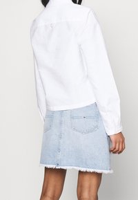 White cropped shirt with long sleeves, back yoke detail; paired with a light blue denim skirt featuring a frayed hem and two back pockets.