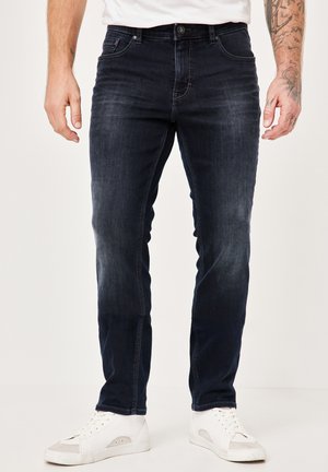 Dunkelblaue Denim-Jeans mit schmaler Passform, die dezente Ausbleichungen, Vordertaschen und einen Knopfverschluss aufweisen, kombiniert mit weißen Turnschuhen.