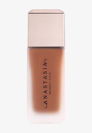 Flacon rectangulaire en verre dépoli avec un fond de teint liquide beige et un bouchon carré rose pâle brillant, étiqueté Anastasia Beverly Hills.