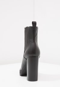 Czarne skórzane botki za kostkę z teksturowanym wierzchem, bocznym zamkiem błyskawicznym i masywnym czarnym obcasem. Posiadają pętelkę z tyłu ułatwiającą zakładanie.