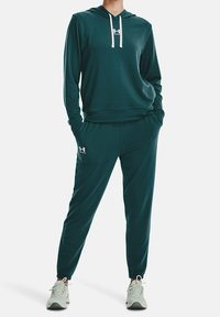 Türkise Kapuzenpullover mit weißen Kordeln und Logo, kombiniert mit passenden Jogginghosen. Weicher, bequemer Stoff mit lässiger Passform und schmal zulaufenden Beinen.