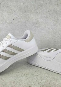 Scarpe da ginnastica bianche con strisce argentate metalliche, tomaia in pelle liscia, dettagli testurizzati e suola ammortizzata, con logo.