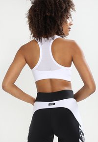 Hvit sportsbh med en pustende mesh rygg, kombinert med svarte leggings som har et hvitt sidepanel og merkevarenavn på livlinen.
