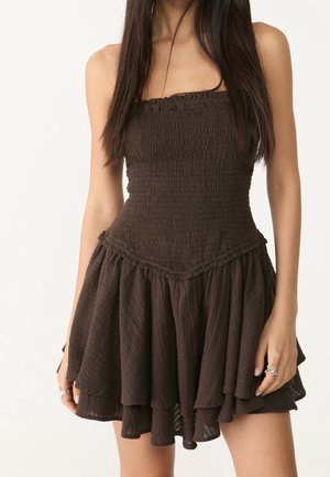 Brązowa, bezrękawnikowa sukienka z dopasowanym gorsetem i warstwową, rozkloszowaną spódnicą. Wykonana z teksturowanej tkaniny z falbankami na krawędziach.