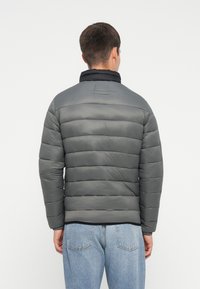 Polstret jakke i mørkegrå med en glat tekstur, der har vandret syninger og en høj krave. Bagsiden viser et enkelt design og stofdetaljer.