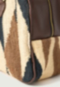 Sac en cuir marron et tissu tissé présentant un motif en zigzag en crème, marron et bleu. Accent de fermeture éclair dorée sur un côté.