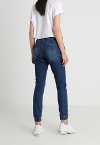 Pantalones jogger de mezclilla azul de corte ajustado con puños elásticos, combinados con una camiseta blanca corta. Textura suave y detalles de costuras minimalistas.