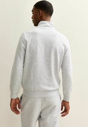 Grauer Fleece-Pullover mit hohem Kragen, gerippten Bündchen und Saum. Glatte Textur, lässiges Design, kombiniert mit passenden Jogginghosen.