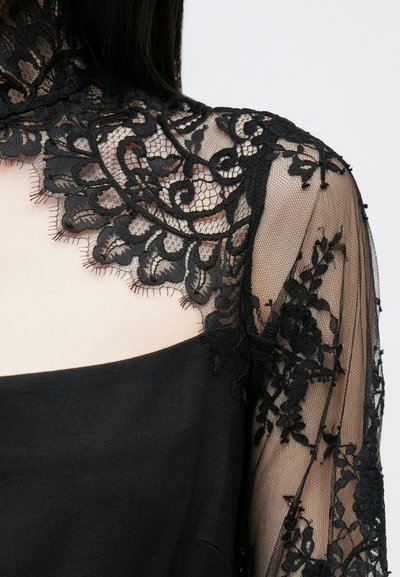 Svart kjole med gjennomsiktig blonder på halsen og ermene, dekorert med blomster. Stoffet er glatt med detaljert broderi og bølgete kanter.