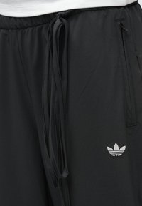 Fekete atlétikai nadrág sima anyagból, elasztikus derékrésszel és húzózsinórral, oldalzsebekkel és egy kis fehér logóval.