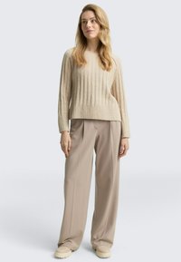 Beige ribbeltrui met lange mouwen, gecombineerd met lichtbeige wijde broek en crèmekleurige instappers.