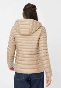 Beige pufferjack met capuchon, voorzien van een gequiltde textuur en een ribbelontwerp. Gladde afwerking en een slim fit, gecombineerd met donkere denim.
