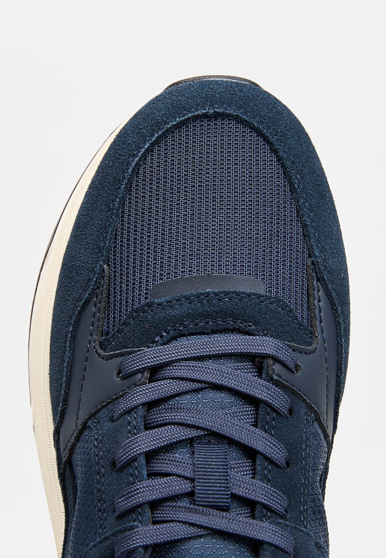 Le sneaker blu navy presentano una combinazione di suede testurizzato e materiale in rete, con un sistema di lacci piatto e una suola in gomma color crema.
