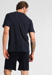 Marineblauw shirt met korte mouwen, voorzien van een klein, overal wit ankerpatroon, gecombineerd met zwarte shorts. Zachte stof met een ontspannen pasvorm.