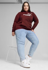 Felpa con cappuccio bordeaux con logo Puma bianco, tasca a marsupio, abbinata a jeans azzurri e sneakers bianche. Tessuto dalla consistenza liscia.