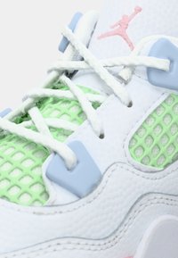 Λευκό αθλητικό παπούτσι με υφή στην επιφάνεια, πράσινες λεπτομέρειες από δίχτυ, γαλάζια οπές και λευκά κορδόνια. Περιλαμβάνει ροζ λογότυπο.