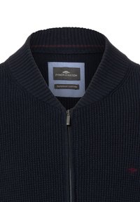 Marineblauer Reißverschluss-Cardigan aus weicher Baumwolle mit gerippter Struktur und hohem Kragen. Markenlabel auf der Innenseite sichtbar.