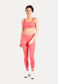 Conjunto de sujetador deportivo rosa y mallas de cintura alta con rayas blancas. Textura suave, tela elástica y diseño ajustado. Zapatillas deportivas blancas.