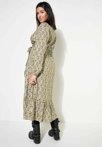 Largo vestido verde con un patrón, con un dobladillo con volantes, cintura ajustada y mangas largas; combinado con botas negras hasta el tobillo.